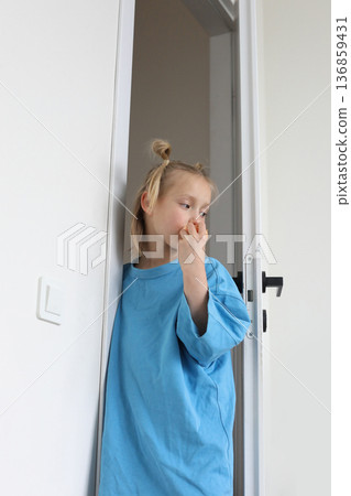 Little child girl stands at white open door and eats tangerine at home Little child girl stands at white open door and eats tangerine at home 136859431