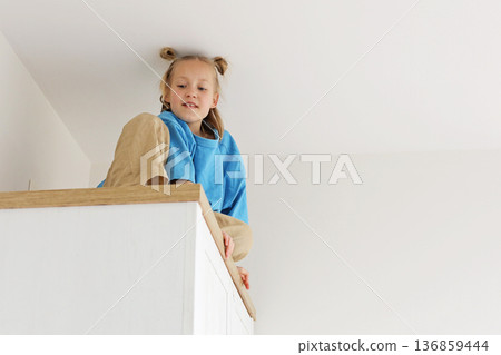 Pretty kid girl sitting on a high cabinet. Child 6 years old at home Pretty kid girl sitting on a high cabinet. Child 6 years old at home 136859444