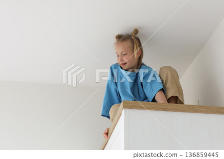 Portrait of young girl climbing on a high cabinet having fun Portrait of young girl climbing on a high cabinet having fun 136859445