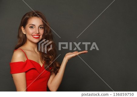Happy model woman holding empty open palm hand and looking at camera on black background Happy model woman holding empty open palm hand and looking at camera on black background 136859750