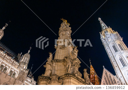 Night view of Fisherman Bastion and church in Budapest's castle district. Illuminated architecture, cobblestone streets, and historic buildings create a picturesque scene. Night view of Fisherman Bastion and church in Budapest's castle district. Illuminated architecture, cobblestone streets, and historic buildings create a picturesque scene. 136859912