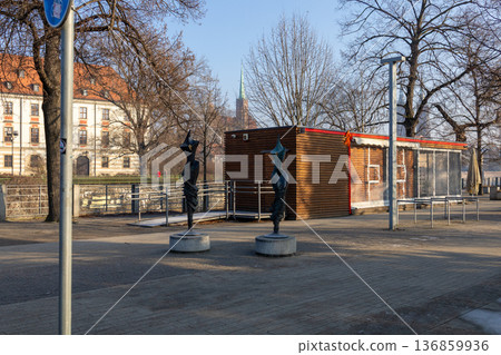 Wooden structure stands by the river with two sculptures on the sidewalk Wooden structure stands by the river with two sculptures on the sidewalk 136859936