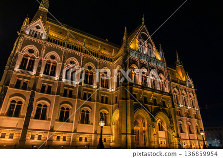 Budapest Parliament building illuminated at night. The architectural details are highlighted by warm lights. A clear sky enhances the scene. Budapest Parliament building illuminated at night. The architectural details are highlighted by warm lights. A clear sky enhances the scene. 136859954