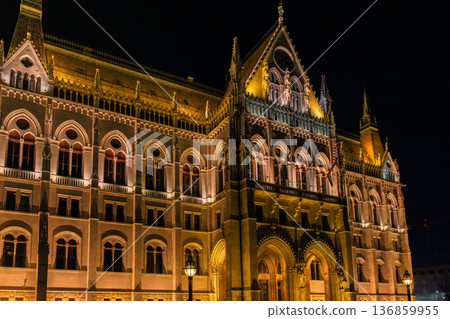 Budapest Parliament building illuminated at night. The architectural details are highlighted by warm lights. A clear sky enhances the scene. Budapest Parliament building illuminated at night. The architectural details are highlighted by warm lights. A clear sky enhances the scene. 136859955