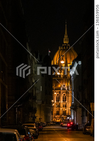 Budapest Parliament building illuminated at night. The architectural details are highlighted by warm lights. A clear sky enhances the scene. Budapest Parliament building illuminated at night. The architectural details are highlighted by warm lights. A clear sky enhances the scene. 136859956