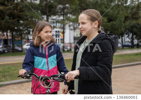 Adorable children girls 10 and 12 years old with bicycle walking outdoors Adorable children girls 10 and 12 years old with bicycle walking outdoors 136860001
