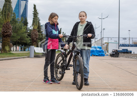 Cute young girls talking and walking together. Children with bikes outdoors 136860006