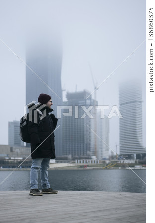 Man in winter coat overlooking a foggy city waterfront. Concept of a city winter activity 136860375