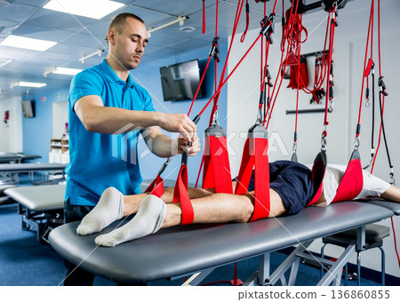 Physiotherapy. Suspension training therapy. Young man doing fitness traction Physiotherapy. Suspension training therapy. Young man doing fitness traction 136860855