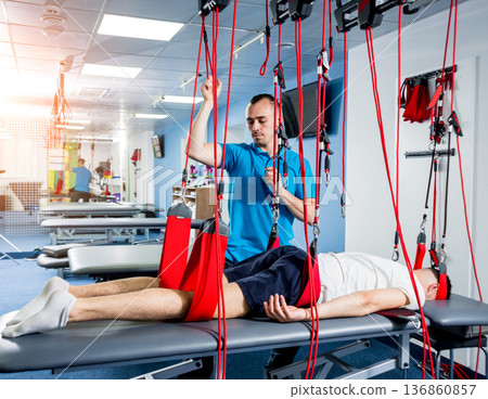 Physiotherapy. Suspension training therapy. Young man doing fitness traction Physiotherapy. Suspension training therapy. Young man doing fitness traction 136860857