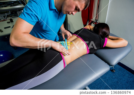Kinesiotaping. Physical therapist applying tape to young beautiful womans spine Kinesiotaping. Physical therapist applying tape to young beautiful womans spine 136860974