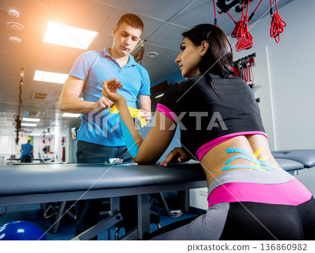 Kinesiotaping. Physical therapist applying tape to young beautiful womans spine Kinesiotaping. Physical therapist applying tape to young beautiful womans spine 136860982