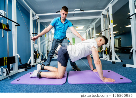 Rehabilitation therapy. Young man doing exercises on mat Rehabilitation therapy. Young man doing exercises on mat 136860985