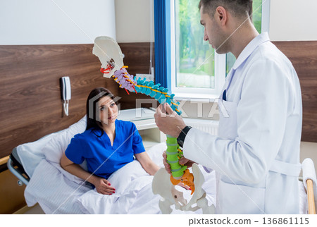 Orthopedist showing spine model to patient in hospital Orthopedist showing spine model to patient in hospital 136861115