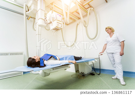 Radiologist and patient in a x-ray room. Classic ceiling-mounted x-ray system. Radiologist and patient in a x-ray room. Classic ceiling-mounted x-ray system. 136861117