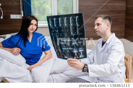 Traumatologist showing MRI film to patient in hospital. Traumatologist showing MRI film to patient in hospital. 136861213