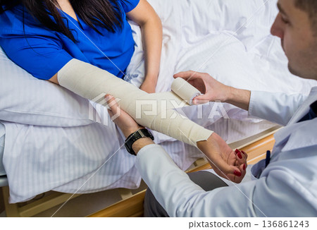 Male doctor bandaging hand of female patients. Male doctor bandaging hand of female patients. 136861243