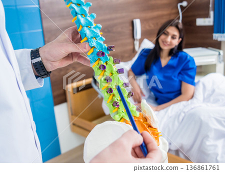 Orthopedist showing spine model to patient in hospital Orthopedist showing spine model to patient in hospital 136861761