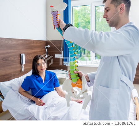 Orthopedist showing spine model to patient in hospital Orthopedist showing spine model to patient in hospital 136861765