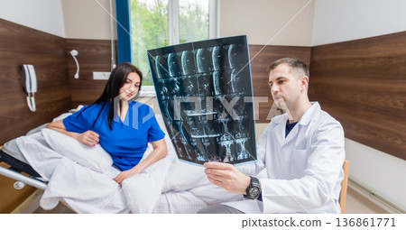 Traumatologist showing MRI film to patient in hospital. Traumatologist showing MRI film to patient in hospital. 136861771