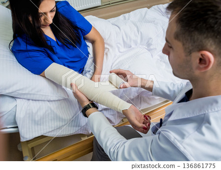 Male doctor bandaging hand of female patients. 136861775