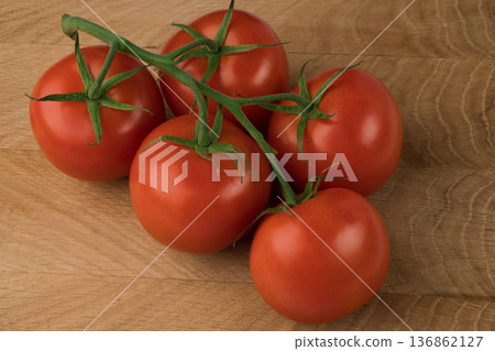 Five red tomatoes on a green branch on a wooden background. 136862127