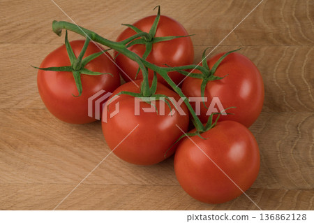 Five red tomatoes on a green branch on a wooden background. 136862128