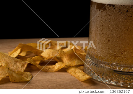 Glass with beer and chips on wood board and black background Glass with beer and chips on wood board and black background 136862167