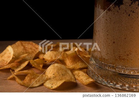 Glass with beer and chips on wood board and black background Glass with beer and chips on wood board and black background 136862169