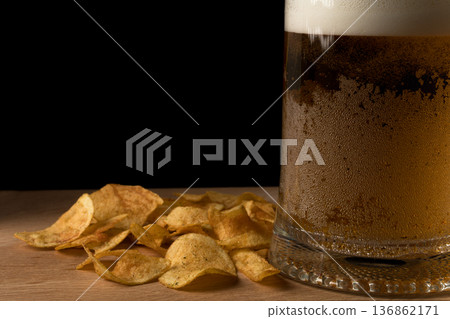 Glass with beer and chips on wood board and black background 136862171
