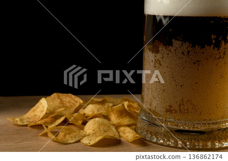 Glass with beer and chips on wood board and black background Glass with beer and chips on wood board and black background 136862174
