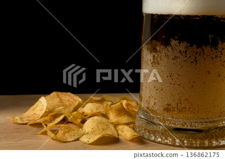 Glass with beer and chips on wood board and black background Glass with beer and chips on wood board and black background 136862175
