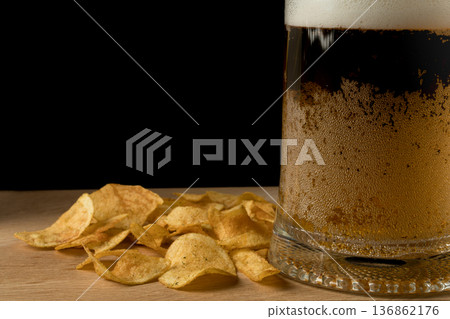 Glass with beer and chips on wood board and black background Glass with beer and chips on wood board and black background 136862176