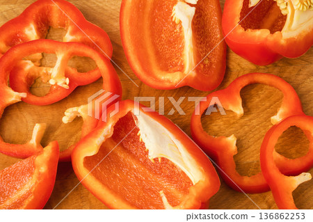 Sliced pieces, parts, lobes of sweet pepper, red, scattered on a wooden board Sliced pieces, parts, lobes of sweet pepper, red, scattered on a wooden board 136862253