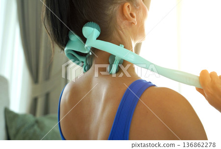 A woman uses a turquoise neck massager after a workout A woman uses a turquoise neck massager after a workout 136862278