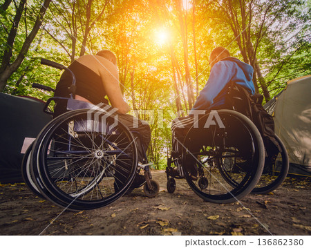 Two disabled men resting in a campsite with friends. Wheelchair in the forest  136862380