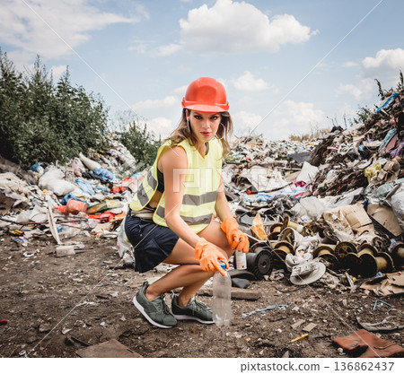 Woman volunteer helps clean the field of plastic garbage.  136862437