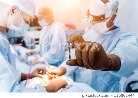 Spinal surgery. Surgeon show polyaxial screw in operating room Spinal surgery. Surgeon show polyaxial screw in operating room 136862444