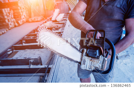 Woodcutter cutting tree with chainsaw on sawmill. Woodcutter cutting tree with chainsaw on sawmill. 136862465