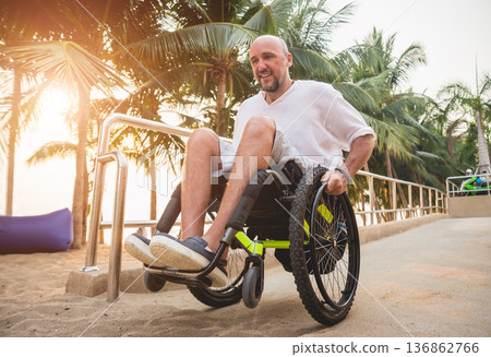 Disabled man in a wheelchair moves on a ramp to the beach. Disabled man in a wheelchair moves on a ramp to the beach. 136862766