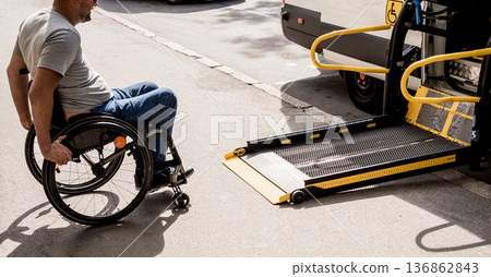 A man in a wheelchair moves to the lift of a specialized vehicle A man in a wheelchair moves to the lift of a specialized vehicle 136862843