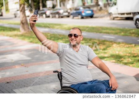 Handicapped man in wheelchair at the park alley use a smartphone 136862847