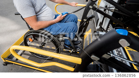 A man in a wheelchair on a lift of a vehicle for people with disabilities A man in a wheelchair on a lift of a vehicle for people with disabilities 136862856
