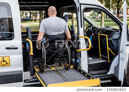 A man in a wheelchair on a lift of a vehicle for people with disabilities A man in a wheelchair on a lift of a vehicle for people with disabilities 136862863