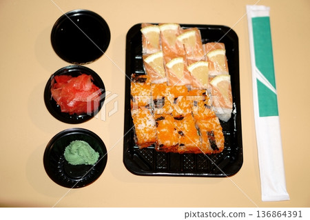 a set of sushi rolls in a plastic container and additional spices in a plastic bowl 136864391