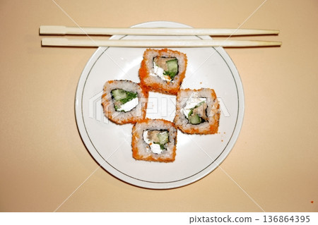 Sushi rolls lie in a white plate on an orange background Sushi rolls lie in a white plate on an orange background 136864395