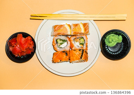 Sushi rolls lie in a white plate on an orange background Sushi rolls lie in a white plate on an orange background 136864396