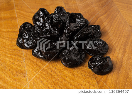 Dried dried prunes in a heap on a wooden board Dried dried prunes in a heap on a wooden board 136864407