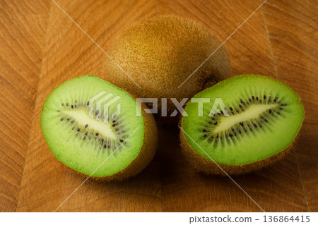 Kiwi one whole and one cut in half lie on a wooden board Kiwi one whole and one cut in half lie on a wooden board 136864415