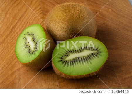 Kiwi one whole and one cut in half lie on a wooden board Kiwi one whole and one cut in half lie on a wooden board 136864416